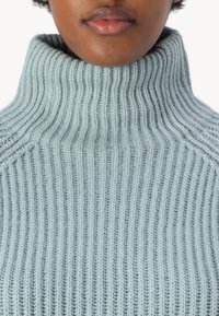 Light blue knitted turtleneck sweater with ribbed texture, featuring a high collar and a fitted design, showcasing vertical stitching details.