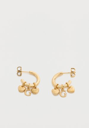 Boucles d'oreilles créoles en or avec trois breloques chacune : deux formes de cœur gravées du mot "GUESS" et une breloque en forme de lettre "G" au centre.