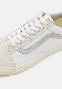 Tenisi albi din pânză cu accente din piele de căprioară gri, șireturi albe plate și talpă din cauciuc texturat. Prezintă un design distinctiv cu dungi pe lateral.