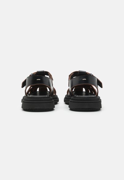 Sandales en cuir noir avec plusieurs sangles, boucles réglables et semelle noire texturée. Design ouvert avec renfort au talon et aux orteils.