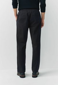 Fekete, rugalmas derekú nadrág laza szabással, két hátsó zsebbel és sima textúrával. Fekete cipővel párosítva.