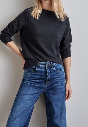 Czarny, teksturowany top z długim rękawem w połączeniu z wysokim stanem, szerokimi spodniami dżinsowymi w kolorze niebieskim, z przodem zapinanym na rozporek oraz srebrnymi dodatkami.