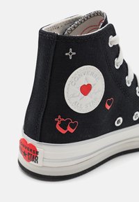 Czarne wysokie trampki Converse z białą podeszwą, wzorami czerwonych serc i gwiazdek oraz białymi sznurowadłami.