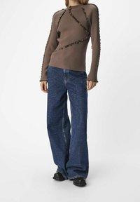 Pull marron côtelé avec des bords à volants, associé à un jean bleu foncé ample avec des motifs usés et des jambes larges. Bottines noires.