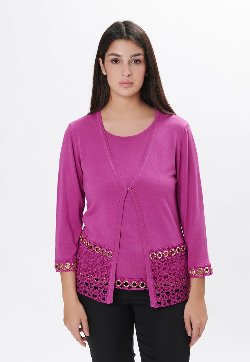 Fuchsia Strickjacke mit Dreiviertelärmeln, verziert mit Spitzenbesatz und goldenen Ösenakzenten am Saum und den Bündchen, kombiniert mit einem passenden Oberteil.