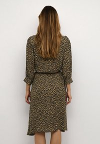 Šaty s leopardím potiskem z polyesteru, s dlouhými rukávy, v pase stažené a s délkou po kolena. Tmavě a světlě hnědý vzor na béžovém pozadí.