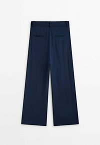Pantalon large bleu marine à la texture lisse, doté d'un devant plat, de deux poches arrière et d'une ceinture à la finition épurée.