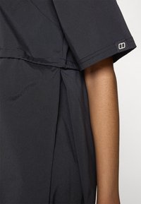 Abito nero realizzato in tessuto morbido, con maniche corte e un sottile dettaglio plissettato. Cuciture visibili e un piccolo accento del marchio.