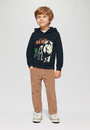 Marinefarbener Hoodie mit Löwengrafik und Text, kombiniert mit braunen Cordhosen. Weiße Sneaker mit grauen Akzenten. Lässiges Kinderoutfit.