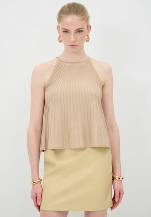 Beige ribbet strik halterneck top med en guldkædeaccent ved halsudskæringen, parret med en lys beige læder mini-sak. Glat tekstur.