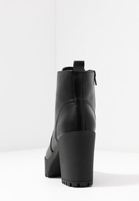 Musta nilkkuri, joka on valmistettu sileästä nahasta, korkea lohko korko ja vetoketjusulkimella takana. Raskaasti muotoiltu kumipohja, joka tarjoaa pitävät otteen.