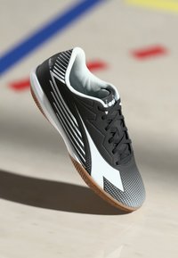 Black and white athletic shoe with rubber sole, textured upper, diagonal stripes, and mesh lining. Features laces and a pronounced toe cap.