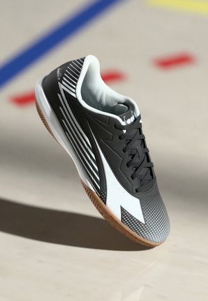 Black and white athletic shoe with rubber sole, textured upper, diagonal stripes, and mesh lining. Features laces and a pronounced toe cap.