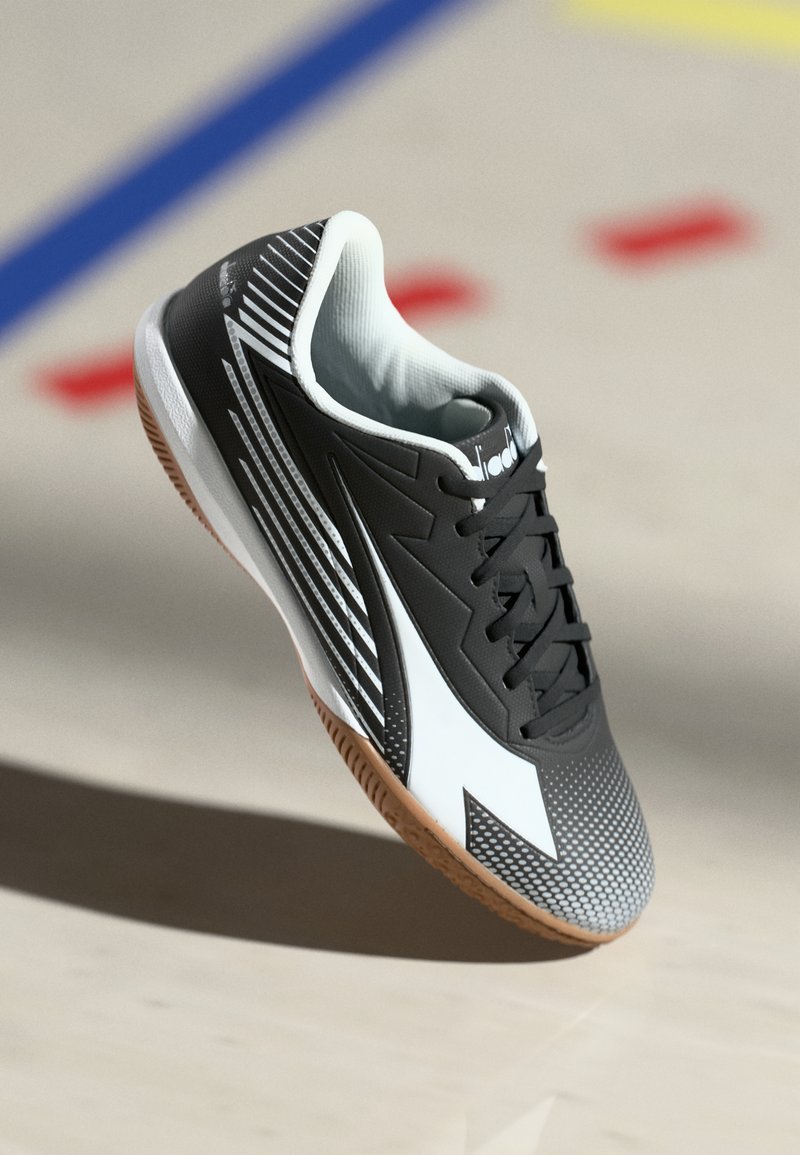 Black and white athletic shoe with rubber sole, textured upper, diagonal stripes, and mesh lining. Features laces and a pronounced toe cap.