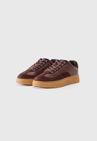Brown suede sneakers with a smooth leather upper, round toe, and gum rubber sole, featuring five eyelets and black inner lining.
