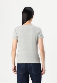 Grå T-shirt med korte ærmer og rund halsudskæring, lavet af en blød tekstur, tætsiddende om taljen, vist på en person der vender væk.