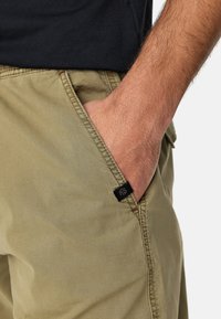 Khaki cotton shorts with a textured finish, featuring a side pocket and a small black label on the left seam. Casual design.