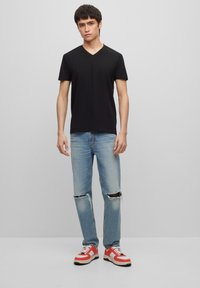 Black v-neck t-shirt, light blue distressed jeans with ripped knees, red and white sneakers with black accents, balanced modern fit.