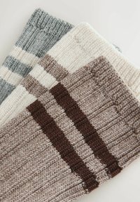 Három kötött lábmelegítő szürke, fehér és bézs árnyalatban, csíkos mintával. Texturált, bordázott kialakítású anyag, sötétbarna részletekkel.