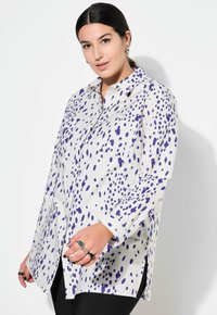Camicia bianca con motivo a macchie viola, maniche lunghe e fessure laterali. Presenta un colletto e una tasca frontale.