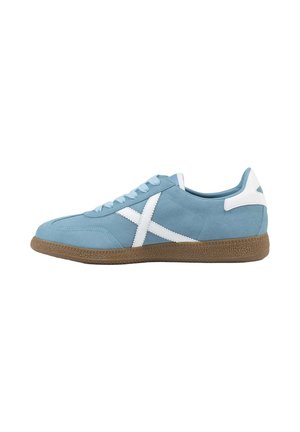 Zapatilla de perfil bajo de ante azul claro con logo lateral blanco en forma de X y suela de goma marrón con textura, vista desde el lado exterior.