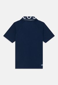 Ναυτικό μπλε πόλο μπλουζάκι από μαλακό ύφασμα, με ριγωτό γιακά και λευκό λογότυπο, κοντά μανίκια, και ευθεία κοπή στο στρίφωμα.