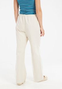 Lichtbeige wijde broek met een elastische tailleband en een gladde textuur, van achteraf weergegeven, met een eenvoudig ontwerp en geen zichtbare patronen.