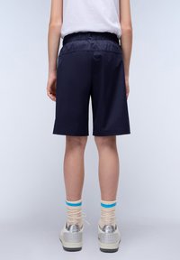 Mörkblå shorts med elastisk midja. Slät tyg, knälång klippning och diskret sömnad. Bärs med krämfärgade strumpor och sportskor.