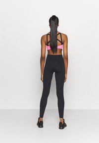 Sportiga svarta leggings som kombineras med en rosa sport-BH med en unik korsad ryggdesign. Släta texturer på båda plaggen.