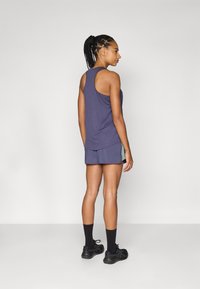 Top de entrenamiento morado con diseño de espalda nadadora, combinado con pantalones cortos a juego que tienen paneles laterales en contraste. Zapatillas deportivas negras y calcetas.