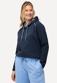 Hoodie cropped marine avec cordons rayés, en tissu doux et avec poches latérales ; associé à un pantalon de jogging bleu clair avec cordon.