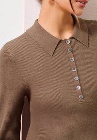 Braunes, geripptes Strickpolohemd mit Kragen und sechs Knöpfen. Der Stoff hat eine glatte Textur und einen subtilen Glanz, der das Design unterstreicht.