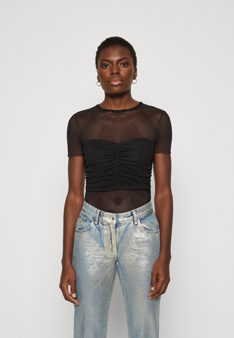 Top negro transparente de manga corta con detalles fruncidos en el frontal, combinado con jeans de tiro alto de acabado metálico en azul claro.