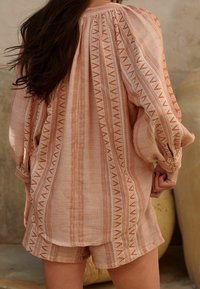 Maglietta a maniche lunghe, morbida, di colore pesca con righe bianche e motivi geometrici, abbinata a pantaloncini corti coordinati, in tessuto testurizzato.