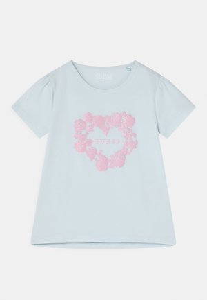 Chemise bleu clair à manches courtes avec motif cœur floral rose et texte "GUESS" au centre devant.