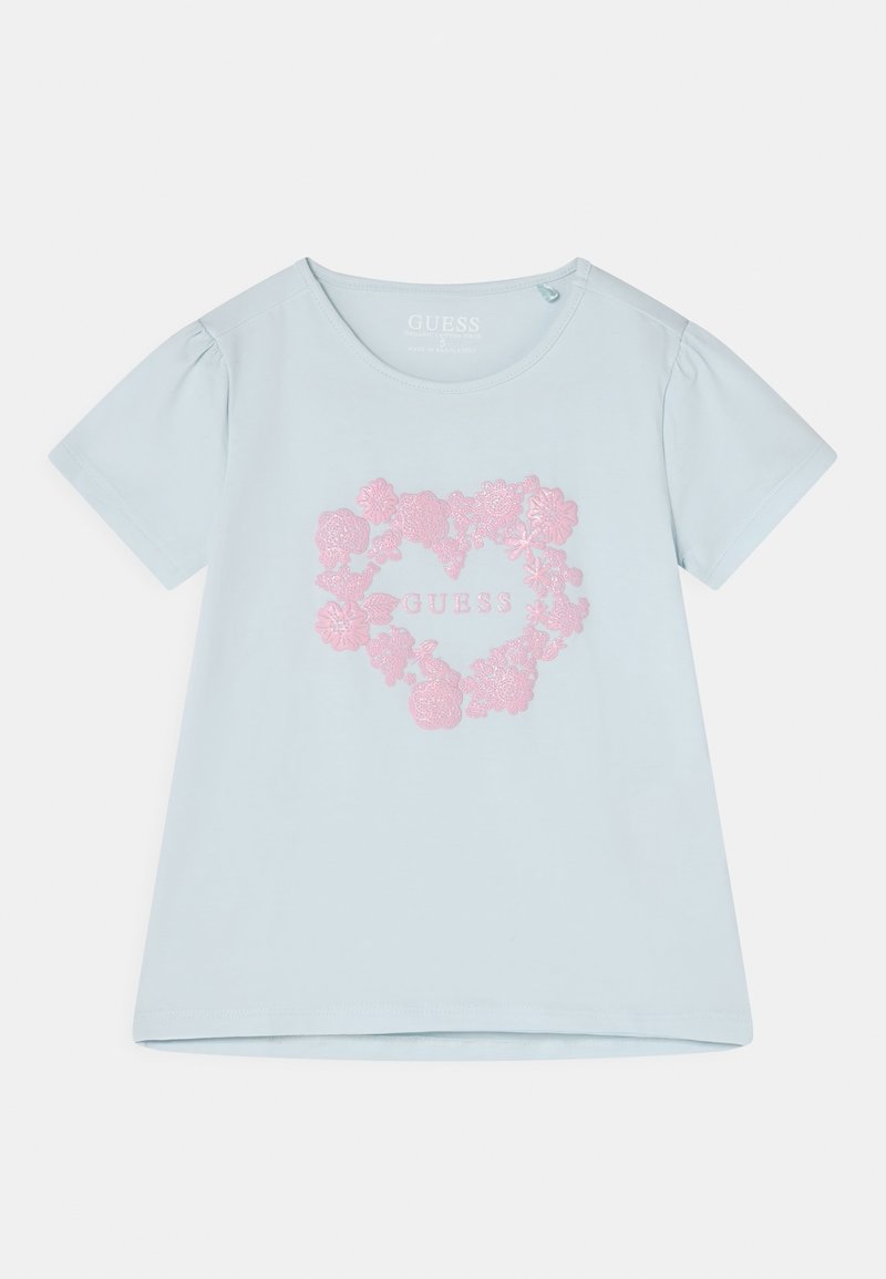 Chemise bleu clair à manches courtes avec motif cœur floral rose et texte "GUESS" au centre devant.