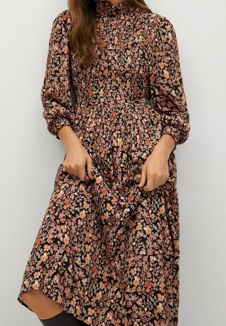 Robe longue à fleurs avec un fond noir orné de petites fleurs orange et crème, taille froncée, col montant et manches bouffantes.
