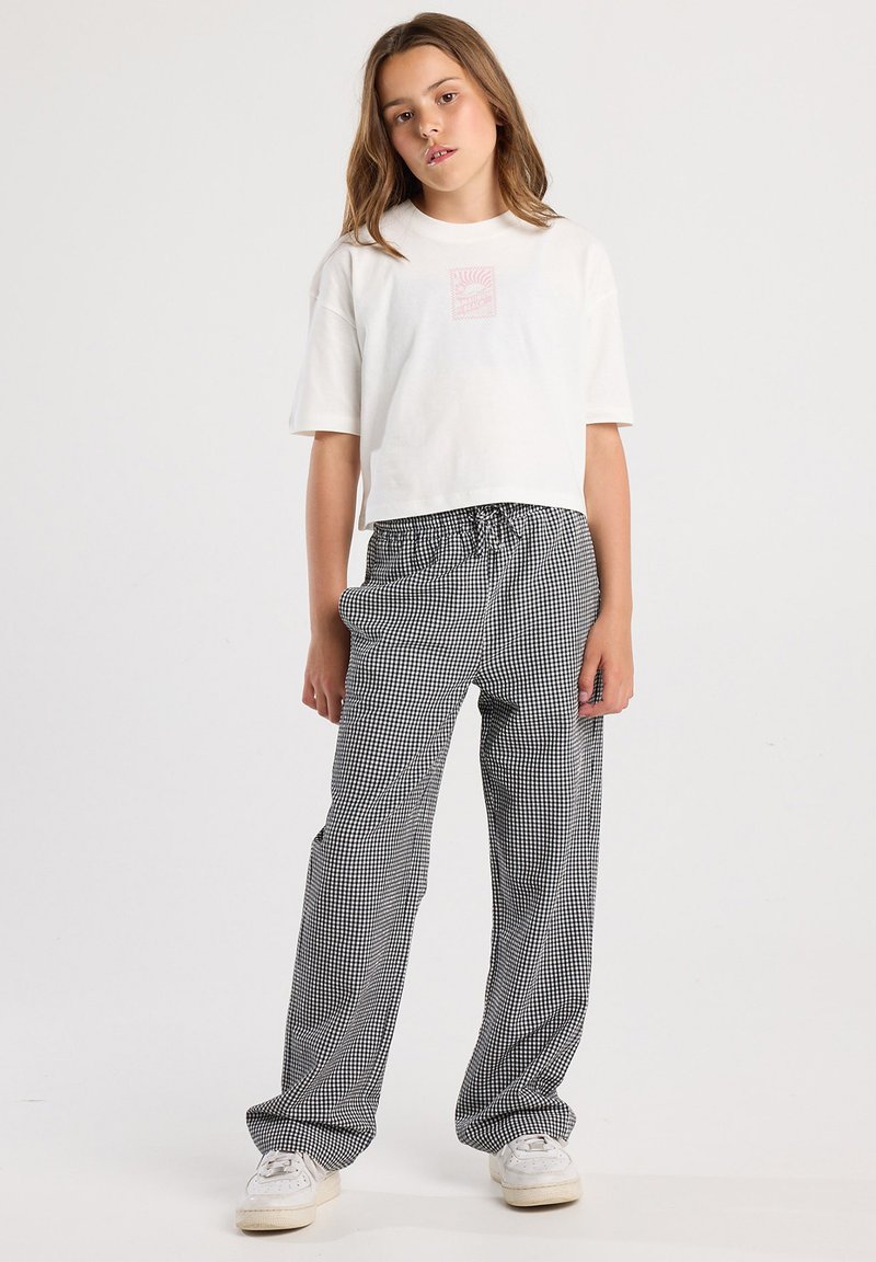White cropped t-shirt with a small pink graphic; black and white gingham check pants with an elastic waistband; white sneakers.