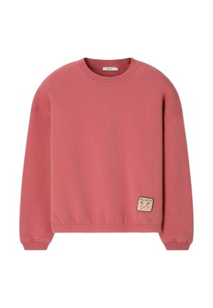 Sweat-shirt rose col rond à manches longues avec un petit patch cousu représentant des palmiers et du texte près de l’ourlet inférieur.