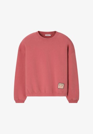 Sweat-shirt rose col rond à manches longues avec un petit patch cousu représentant des palmiers et du texte près de l’ourlet inférieur.