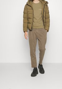 Giubbotto imbottito verde oliva, indossato sopra un felpa coordinata, abbinato a pantaloni in corduroy marrone chiaro e scarpe chunky nere.