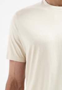 Lichtbeige t-shirt met korte mouwen, gemaakt van zachte stof, met een ronde halslijn en minimale stikdetails op de manchetten en de onderrand.