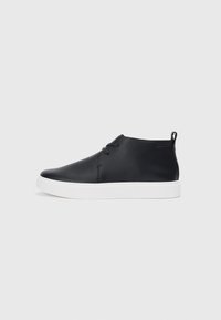 Adidași negri din piele, cu vârf înalt, finisaj neted, talpă din cauciuc alb și un design simplu cu șireturi. Au un tab de prindere în partea din spate.