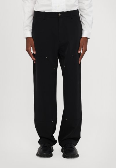 Pantalones negros de corte holgado con una textura suave, que presentan botones a presión visibles y costuras reforzadas en las rodillas.