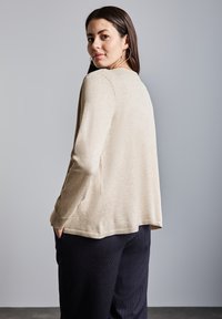 Beige långärmad topp med rund hals, med en lös passform och ribbad fåll. Buren över mörka randiga byxor, med en enkel design.