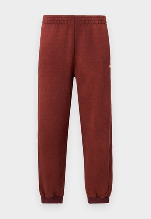 Rozsda színű bolyhos melegítőnadrág, gumírozott derékkal és bokánál szűkítéssel, fehér háttér előtt bemutatva.