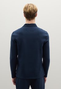 Marineblaue Langarmbluse mit lockerem Schnitt, glatter Textur und dezentem Kragen. Verfügt über eine ordentliche Rückennaht und einen geraden Saum.