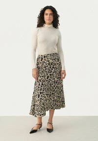Krämfärgad täckkrage som kombineras med en flödande, leopardmönstrad maxikjol i beige och svart, kompletterad med svarta pumps med spetstå. 