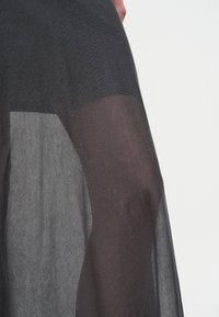 Nærbilde av en person som har gjennomsiktig svart stoff over lår og hofte, som fremhever den gjennomsiktige teksturen og fall.