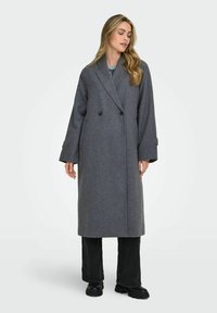 Long grey wool coat with a double-breasted front, oversized sleeves, and side pockets, paired with black wide-leg pants and chunky black boots.